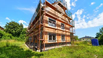 Neubau im Rohbauzustand mit Gerüst und blauer Baustellentoilette unter blauem Himmel.