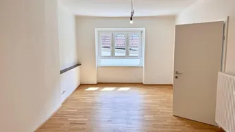 Helles Zimmer mit Parkettboden, weißen Wänden und einem Fenster, das Tageslicht hereinlässt.