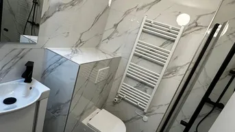 Modernes Badezimmer mit Marmorfliesen, Duschkabine, Wand-WC und beheiztem Handtuchhalter.