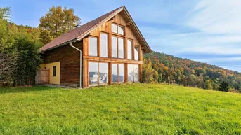Holzhaus mit großen Fensterfronten und weitem Blick über die grüne Hügellandschaft.
