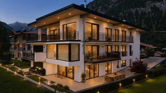 Modernes Mehrfamilienhaus bei Abenddämmerung mit beleuchteten Terrassen und Balkonen vor Bergkulisse.