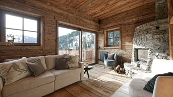 Gemütliches Wohnzimmer im alpinen Stil mit Holzwänden, Steinkamin und Panoramablick auf die verschneiten Berge.