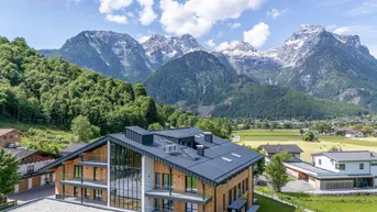 Modernes Gebäude mit Holzfassade und dunklem Dach, eingebettet in eine grüne Landschaft mit majestätischen Bergen im Hintergrund.