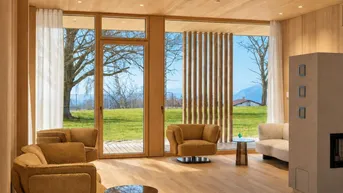 Lichtdurchflutetes Wohnzimmer mit Holzboden, modernen Sesseln und Kaminofen mit Blick ins Grüne.