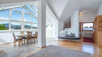 Heller Wohn- und Essbereich mit großen Glasflächen, Bergblick und Holzboden im Dachgeschoss.