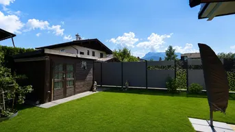 Gepflegter Gartenbereich mit Rasenfläche, Gartenhaus und Blick auf die umliegende Berglandschaft.