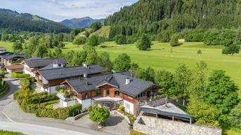 Luftaufnahme eines luxuriösen Chalets mit traditioneller Holzfassade und Blick auf grüne Hügel und Berge.