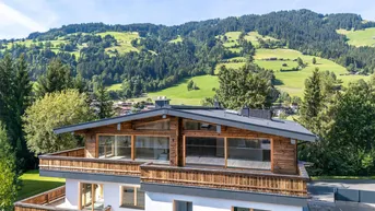 Modernes Chalet mit Holzbalkonen und großen Fenstern vor einer grünen Berglandschaft.