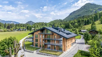 Modernes Apartmentgebäude mit Holzfassade und großen Glasfronten, eingebettet in eine grüne Berglandschaft.