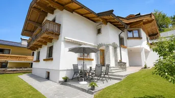 Charmantes Haus im alpinen Stil mit weißer Fassade, Holzdetails und einer gemütlichen Terrasse mit Gartenmöbeln.