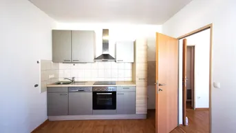 Helle Küche mit Einbauküche, Holzfußboden und Zugang zu einem weiteren Raum.