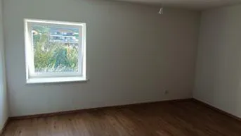 Leerer Raum mit Laminatboden und Fenster, bietet einen Blick ins Grüne und viel Tageslicht.