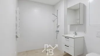 Modernes Badezimmer mit ebenerdiger Dusche, Waschtisch und beheiztem Handtuchhalter in hellen Farbtönen.