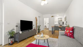 Helles Wohnzimmer mit Sofa, Fernseher und offenem Übergang zum Essbereich und zur Küche.