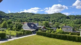 Panoramablick auf grüne Hügel und umliegende Häuser unter blauem Himmel.