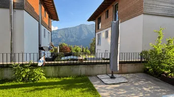 Gepflegter Gartenbereich mit Terrasse und Blick auf die umliegenden Berge, umgeben von modernen Gebäuden.