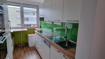 Moderne Küche mit weißen Schränken, Holztheke, grüner Rückwand und Fenster mit Blick nach draußen.