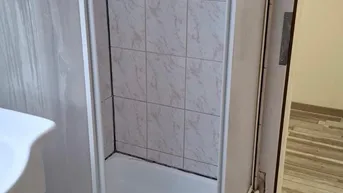 Duschkabine mit weißen Fliesen und einem Waschbecken in einem Badezimmer.