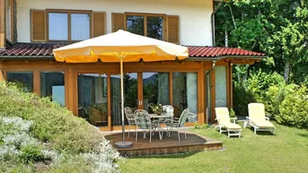 Gemütliche Holzterrasse mit Gartenmöbeln und Sonnenschirm, umgeben von einem gepflegten Garten.