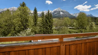 Blick vom Holzbalcon auf die majestätische Berglandschaft und die umliegende grüne Natur.