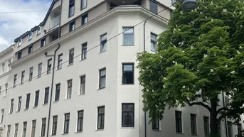 Modernes Eckgebäude mit mehreren Etagen, Balkonen und Geschäften im Erdgeschoss an einer belebten Straße.