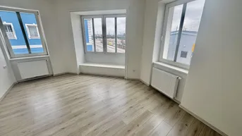 Heller Raum mit modernem Laminatboden, weißen Wänden und großen Fenstern mit Heizkörpern.