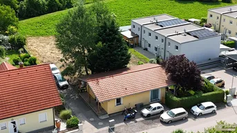 Luftaufnahme eines Einfamilienhauses mit rotem Ziegeldach und umliegender grüner Landschaft.