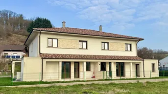 Rückansicht des modernen Hauses mit großen Fenstern und Zugang zum Gartenbereich.