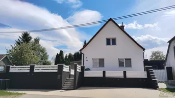 Vorderansicht eines weißen Einfamilienhauses mit rotem Ziegeldach und moderner Zaunanlage.