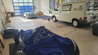 Geräumige Garage mit mehreren Fahrzeugen, darunter ein Oldtimer und ein Transporter, sowie hohen Decken.
