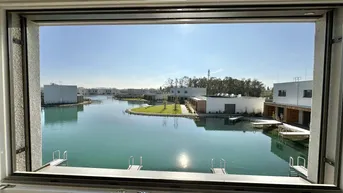 Panoramablick aus dem Fenster auf die ruhige Seenlandschaft und die modernen Häuser der Siedlung.