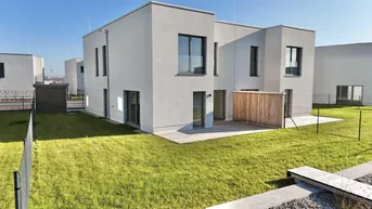 Modernes Doppelhaus mit Garten, Terrasse und großen Fenstern in einer neuen Wohnsiedlung.