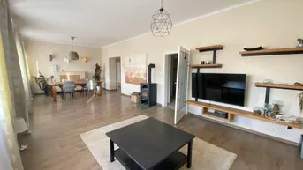 Gemütlicher Wohn-Essbereich mit Holzboden, Kaminofen und modernen Regalen an der Wand.