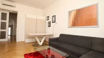 Helles Wohnzimmer mit modernem Sofa, Glastisch und Fischgrätparkettboden.