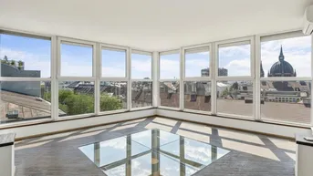 Helles Zimmer mit großen Fenstern, Stadtblick und einem Glasboden, der Licht in die darunterliegende Etage lässt.