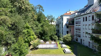 Gepflegter Gemeinschaftsgarten mit Rasenflächen und Bäumen, umgeben von Wohngebäuden.