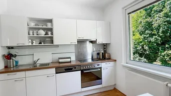 Funktionale Küche mit weißen Schränken, Holz-Arbeitsplatte und Fenster mit Blick ins Grüne.