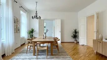 Heller Essbereich mit Holztisch, Parkettboden und hohen Fenstern, der zu weiteren Räumen führt.