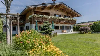 Charmantes Chalet mit Holzbalkonen, blühenden Blumenkästen und gepflegtem Gartenbereich.