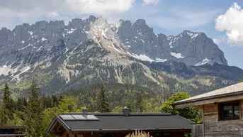 Dach eines Hauses mit Photovoltaikanlage vor einer beeindruckenden Bergkulisse an einem sonnigen Tag.