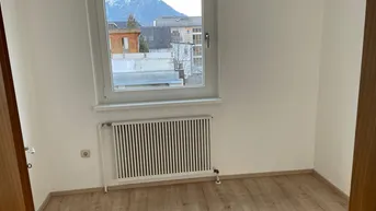 Lichtdurchflutetes Zimmer mit Laminatboden, Heizkörper und Bergblick.