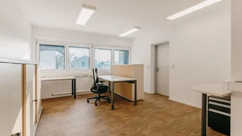 Helles und geräumiges Büro mit mehreren Arbeitsplätzen, großen Fenstern und funktionalen Möbeln.