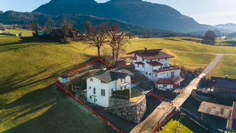 Luftaufnahme des Hauses mit umliegender grüner Landschaft und Bergen im Hintergrund.