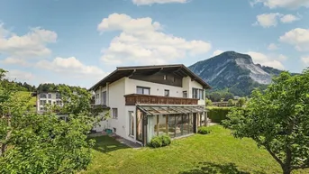 Freistehendes Haus mit Wintergarten, großem Garten und beeindruckendem Bergblick unter blauem Himmel.