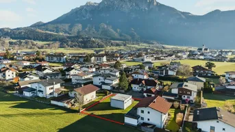 Luftaufnahme eines Baugrundstücks in einer Wohnsiedlung mit beeindruckendem Bergpanorama im Hintergrund.