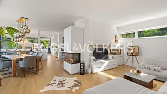 Offener Wohn- und Essbereich mit modernem Kamin, Holzboden und großen Fenstern.