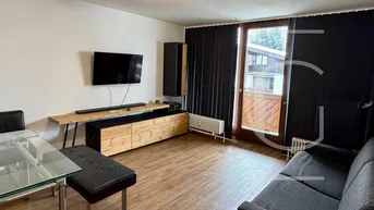 Helles Wohnzimmer mit Holzboden, TV-Möbeln und Zugang zu einem Balkon mit Blick ins Grüne.