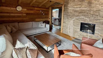 Gemütliches Wohnzimmer im Chalet-Stil mit Holzwänden, Kamin und bequemer Sitzecke.
