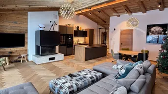 Geräumiger offener Wohn-Essbereich mit moderner Küche, Kamin und Holzbalkendecke.