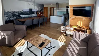 Heller Wohnbereich mit bequemen Sofas, Holzboden und Blick auf den Ess- und Küchenbereich.